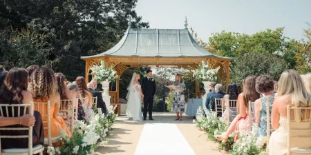 A bride and groom standing with their celebrant - Sam White - underneath the pagoda at Clevedon Hall.