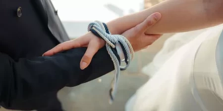 A close-up shot of the knot and the cords around a couples wrists during a modern handfasting ceremony.
