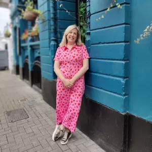 A woman in a pink jumpsuit leaning against a blue wall