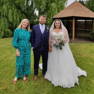 A wedding celebrant stood with a groom and bride