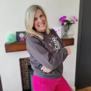 A woman stood smiling wearing pink trousers