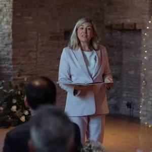 A woman stood in a function room speaking holding a ceremony folder