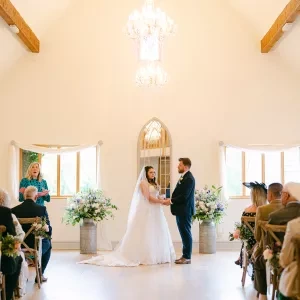 A bride and groom standing at the front of a barn with a celebrant mid-ceremony.